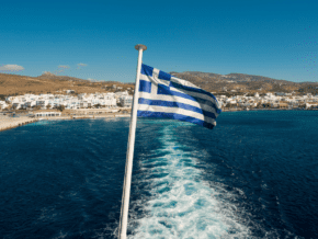 Greek flag on the back of a boat. Motorboat wake leads back to shore